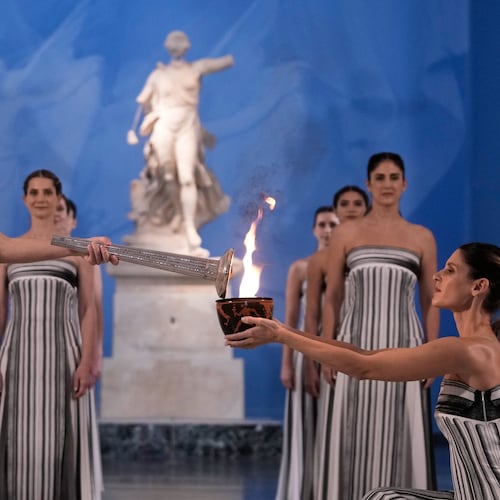 High Priestess Mary Mina, left, lights a torch from the Olympic flame during the flame lighting ceremony for the Milan Cortina 2026 Winter Olympics, at the archaeological museum of Olympia, Greece, Wednesday, Nov. 26, 2025. (AP Photo/Thanassis Stavrakis)