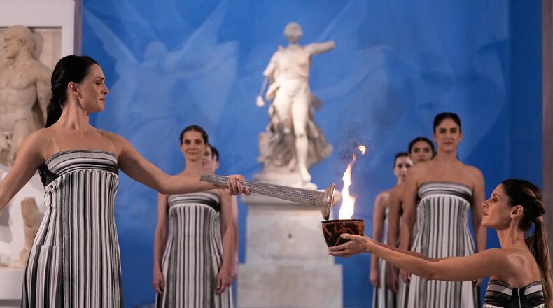 High Priestess Mary Mina, left, lights a torch from the Olympic flame during the flame lighting ceremony for the Milan Cortina 2026 Winter Olympics, at the archaeological museum of Olympia, Greece, Wednesday, Nov. 26, 2025. (AP Photo/Thanassis Stavrakis)