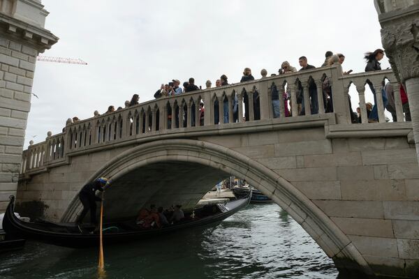 Tourists take pictures in San Marco square in Venice, Italy, Friday, April 18, 2025, Venice on Friday launches for a second year a pilot program to charge day-trippers an entrance fee. (AP Photo/Antonio Calanni)
