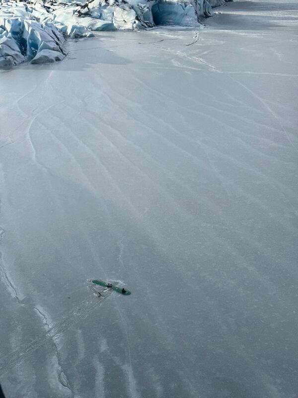 This photo provided Monday, March 24, 2025 by Dale Eicher shows an airplane partially submerged into the ice of Tustumena Lake near Soldotna, Alaska, with the three survivors standing on the plane's wing. (Dale Eicher via AP)