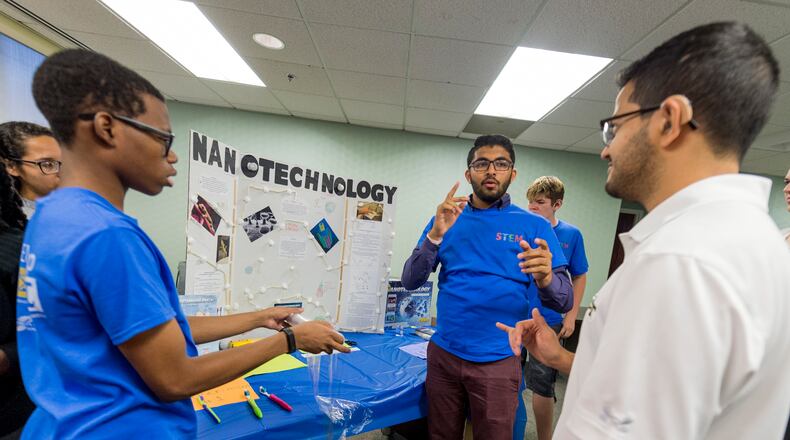 Teens Jared Brown, Dhruvesh Patel and Rafael Montez (l-r blue shirts) explain their nanoscience project to guests during the finale of GSU’s STEM camp for deaf students.