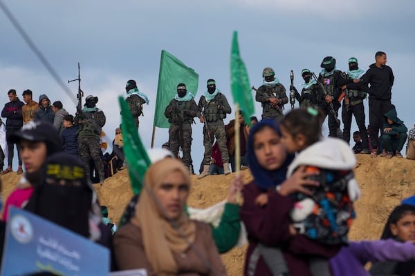 FILE - Palestinians watch as Hamas fighters take up a position ahead of handing over four bodies to the Red Cross in Khan Younis, southern Gaza Strip, Thursday, Feb. 20, 2025.(AP Photo/Abdel Kareem Hana, File)
