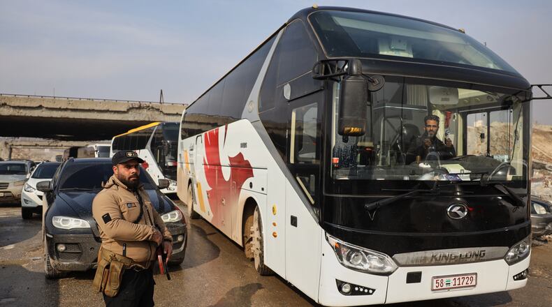Members of Syrian government forces stand around buses prepared to evacuate Kurdish militants, under escort to the country's northeast, controlled by the SDF, after a ceasefire was announced following days of clashes in the northern city of Aleppo, Syria, Friday, Jan. 9, 2026. (AP Photo/Omar Albam)