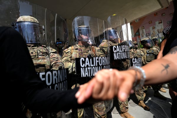 Protesters clasp hands in front of a line of California National Guard, Monday, June 9, 2025, at a Federal Building in downtown Los Angeles. (AP Photo Jae Hong)