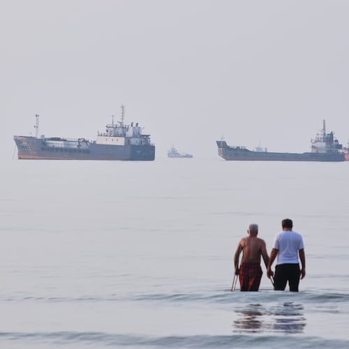 Two men wade in the waters of the Strait of Hormuz with vessels anchored in the background, off Bandar Abbas, Iran, Sunday, July 12, 2026. (Razieh Poudat/ISNA via AP)