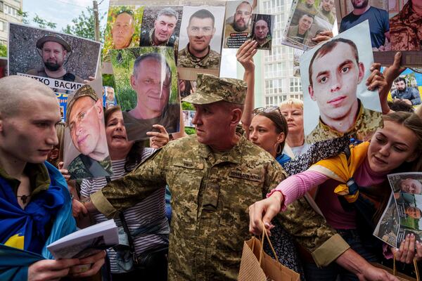 An Ukrainian soldier, left, walks though human corridor with people holding photos of their missed relatives after returning from captivity after a POWs exchange between Russia and Ukraine, in Chernyhiv region, Ukraine, Monday, June 9, 2025. (AP Photo/Evgeniy Maloletka)