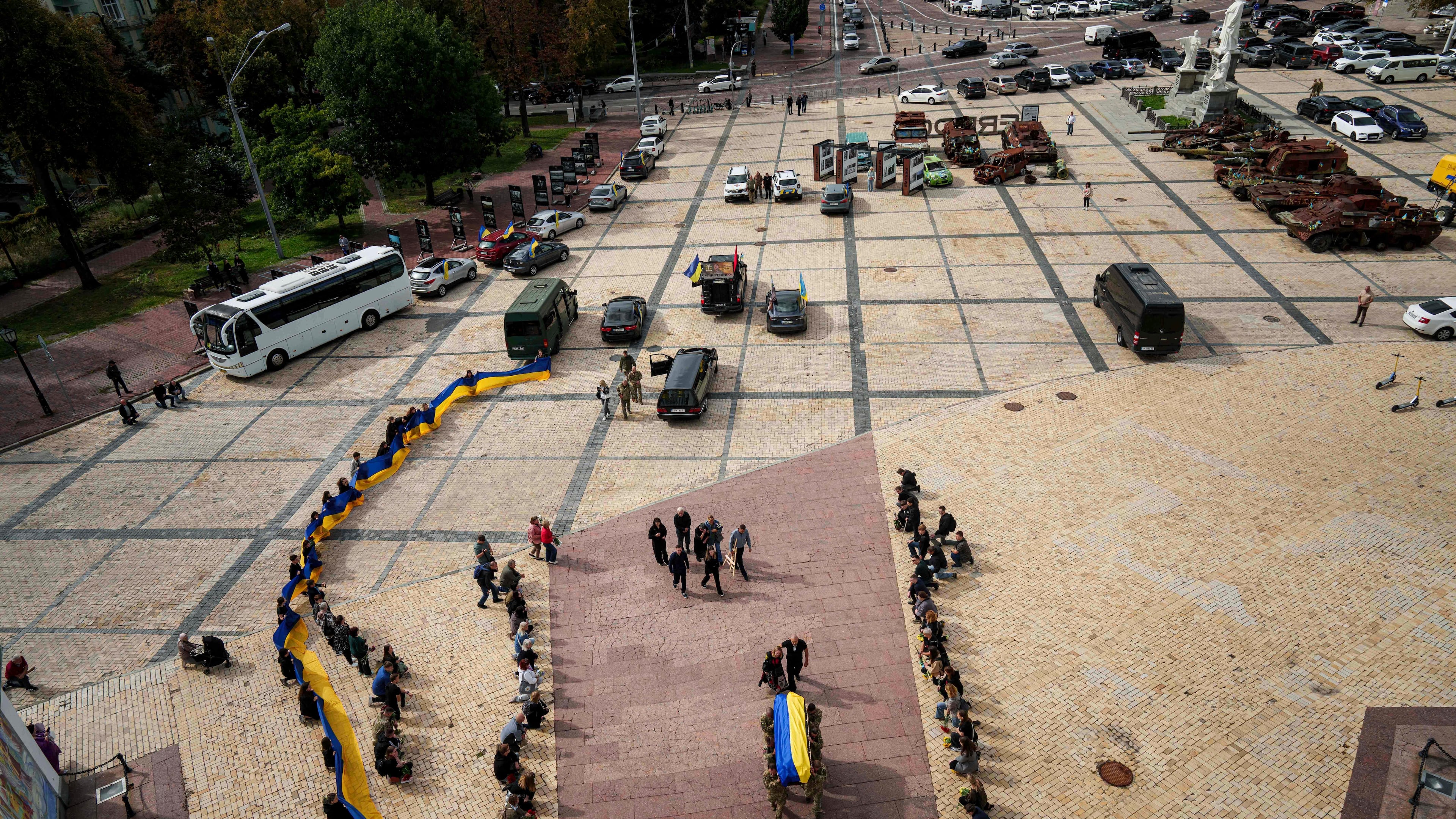 People kneel down, as honor guards carry the coffin of Artem Antonenko, a Ukrainian serviceman, during his funeral ceremony in the center of Kyiv, Ukraine, Friday, Sept. 19, 2025. (AP Photo/Evgeniy Maloletka)