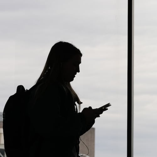 FILE - A traveler with a smartphone walks past an air traffic control tower at Philadelphia International Airport in Philadelphia on March 27, 2026. (AP Photo/Matt Rourke, File)