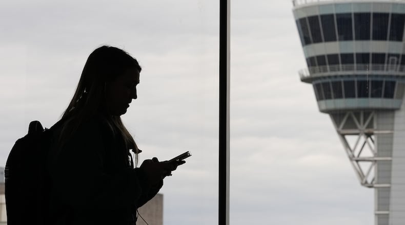 FILE - A traveler with a smartphone walks past an air traffic control tower at Philadelphia International Airport in Philadelphia on March 27, 2026. (AP Photo/Matt Rourke, File)
