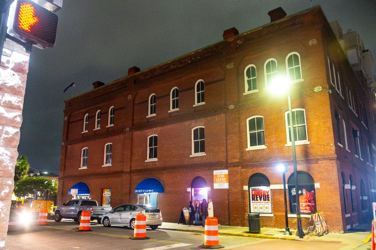 An old brick industrial building with a street lamp in front of it lighting it at night.