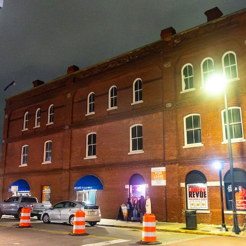 An old brick industrial building with a street lamp in front of it lighting it at night.