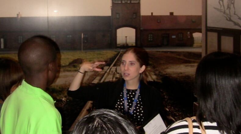 Volunteer Beth Brown, standing in front of a photo of the Auschwitz-Birkenau concentration camp, explains the Holocaust to students from Columbus High School recently at the William Breman Jewish Heritage and Holocaust Museum in the downtown area.