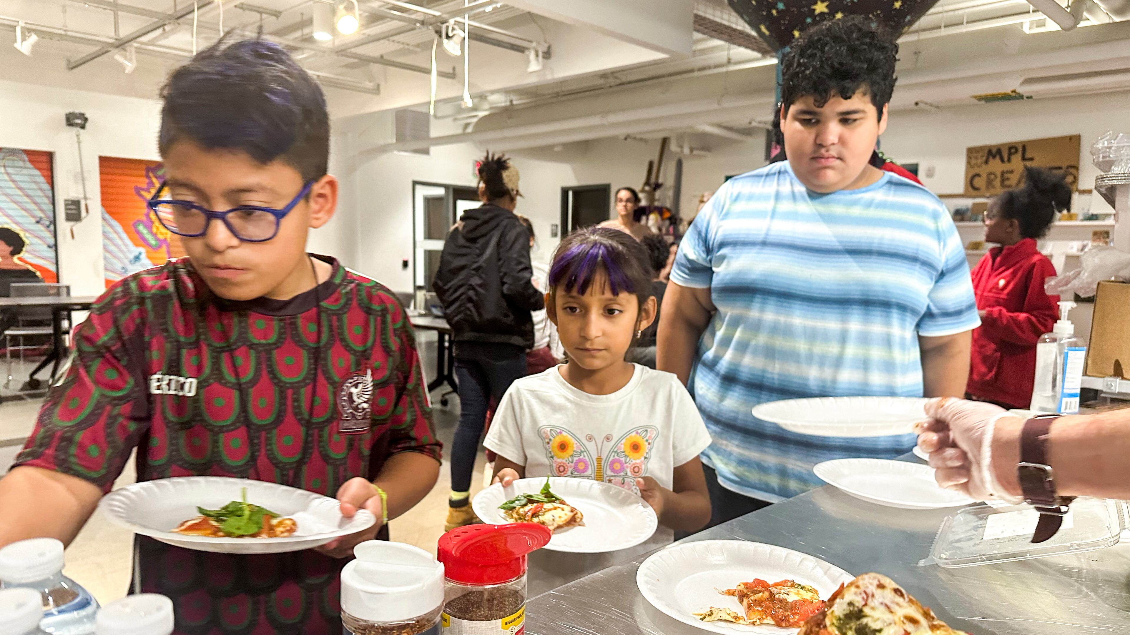 FILE - Attendees of the after school nutrition program, Milwaukee Public Library Snack Hack, line up to get a slice of pizza made from scratch, Nov. 19, 2024, in Milwaukee. (AP Photo/Devi Shastri, File)