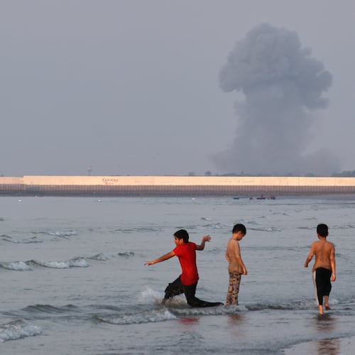 Three boys play in the shallow waters of the Strait of Hormuz, as a plume of smoke rises from an explosion in the background, off Bandar Abbas, Iran, Monday, July 13, 2026. (Razieh Poudat/ISNA via AP)