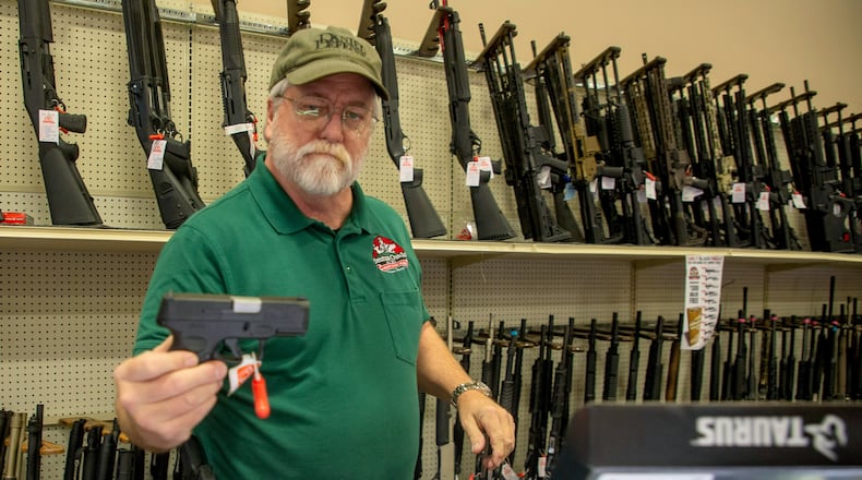 Salesman Hugh Jeffries hands a Taurus handgun to a customer at Adventure Outdoors in Smyrna, Monday, December 13, 2021. STEVE SCHAEFER FOR THE ATLANTA JOURNAL-CONSTITUTION