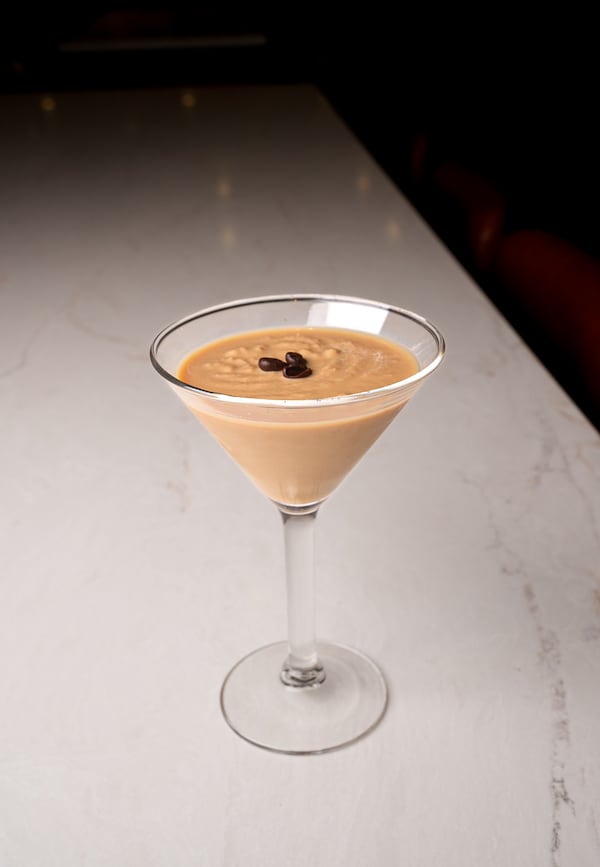 A frozen espresso martini is garnished with three espresso beans. It is in the traditional martini glass and shown on a marble-looking tabletop.