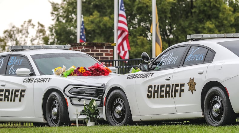 September 12, 2022 Atlanta: A memorial of two patrol cars parked with flowers and notes affixed against a backdrop of flags were lowered to half-staff at the Cobb County Sheriff's Office Adult Detention Center on Monday, Sept. 12, 2022 located at 1825 County Services Parkway in Marietta served as a reminder of the tragedy last week of two Cobb County deputies killed in the line of duty. (John Spink / John.Spink@ajc.com)
