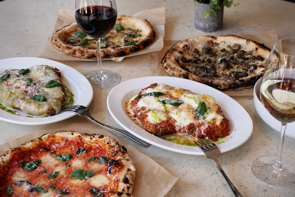 A table full of Italian dishes, including multiple pizzas, pastas and a glass of red wine