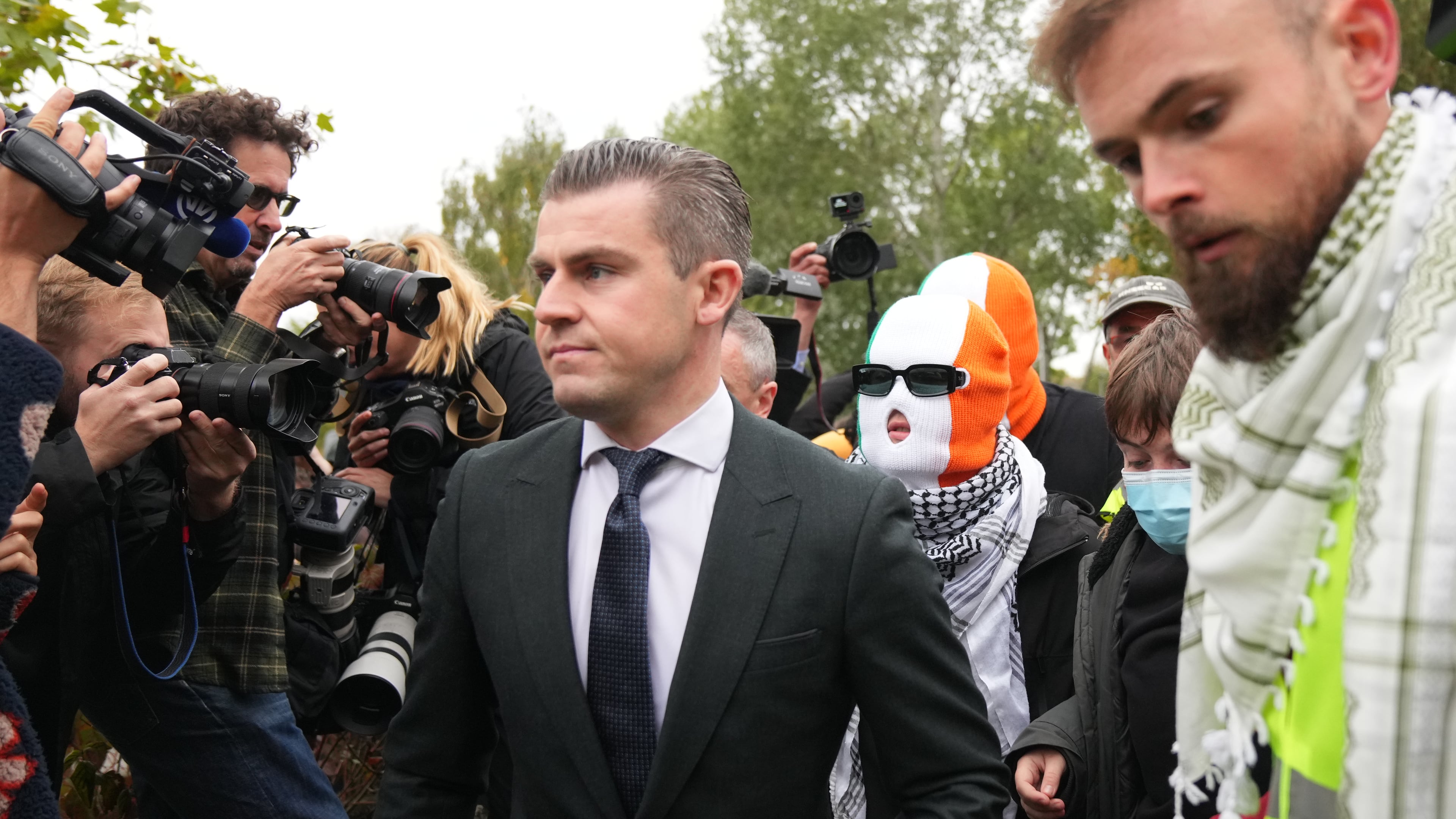 A person believed to be Liam Óg Ó hAnnaidh, aka Mo Chara, in a mask, a member of the Irish language band Kneecap, arrives at Woolwich Crown Court in London London, Friday, Sept. 26, 2025, where he is charged with a terrorism offence relating to displaying a flag in support of Hezbollah during a performance with the band in November 2024. (AP Photo/Joanna Chan)