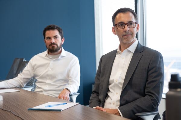 Joe Austin, left, and Matthew Dodge, both with the Federal Defender Program, listen as their client Sam Tunick speaks with a reporter Thursday, July 30, 2026. (Ben Gray for the AJC)
