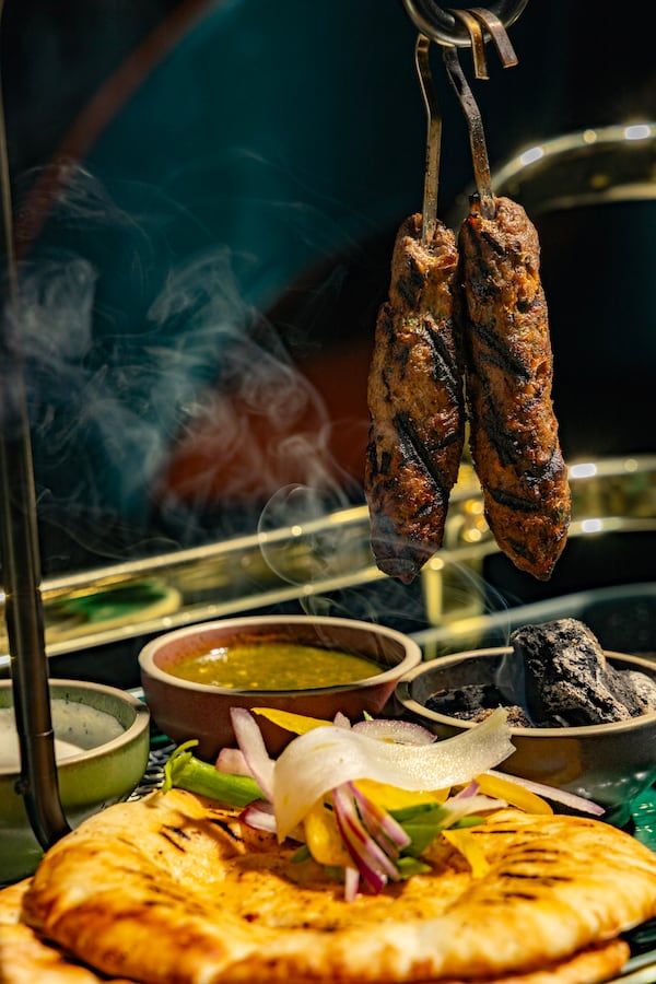 Skewers of grilled chicken hang above a table set with sauces, spreads and a stack of pita bread