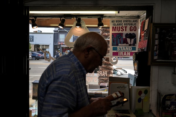 Sam Beykzadeh works in his bookstore in the "Tehrangeles" neighborhood of Los Angeles Tuesday, June 24, 2025, as a poster in the window calls for regime change in Iran. (AP Photo/Jae C. Hong)