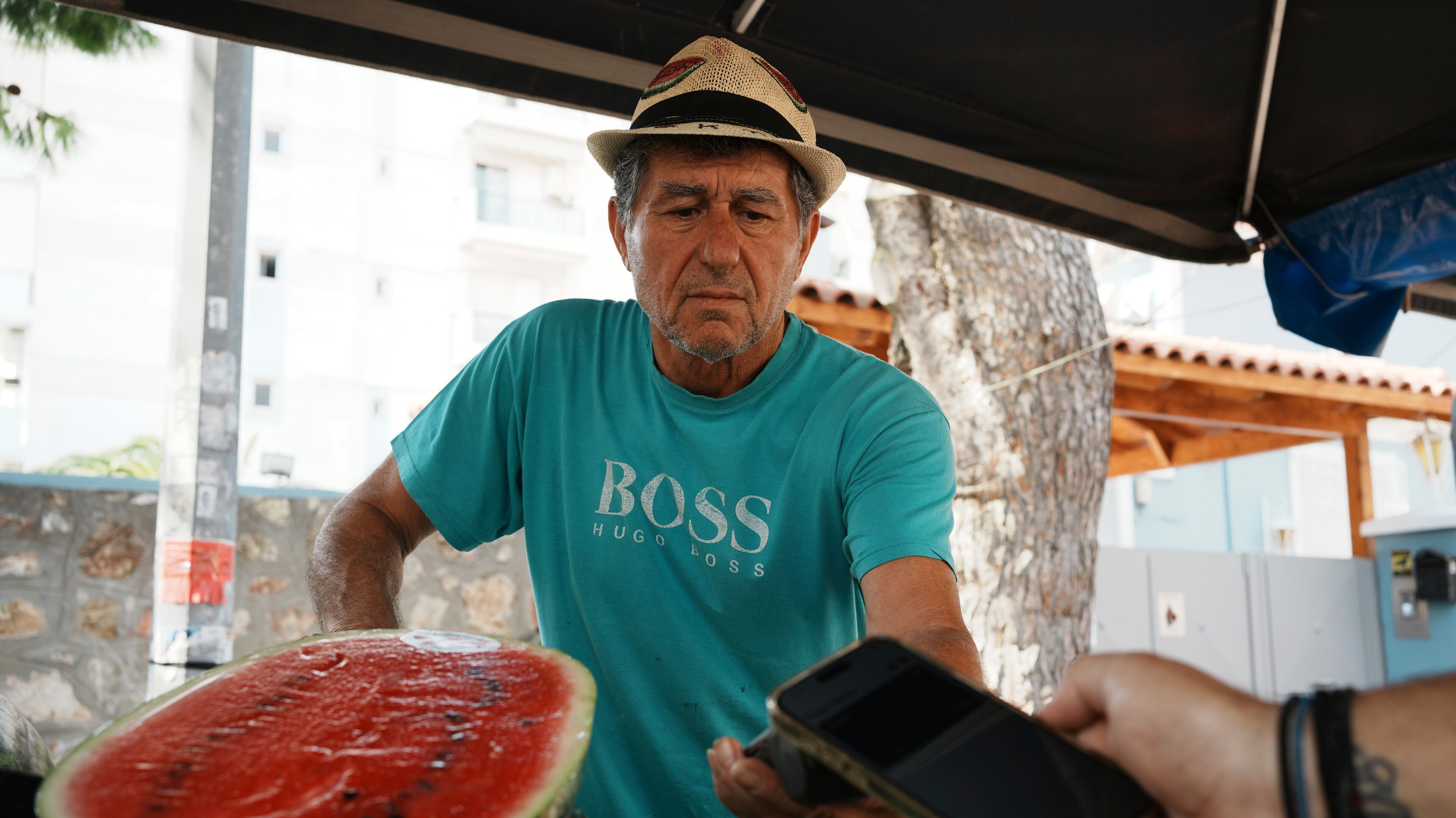 Fruit vendor Makis Panaretos uses a POS terminal for a customer who pays with his cellphone at an open-air fruit and vegetable market in Athens, Greece, Friday, Sept. 5, 2025. (AP Photo/Thanassis Stavrakis)