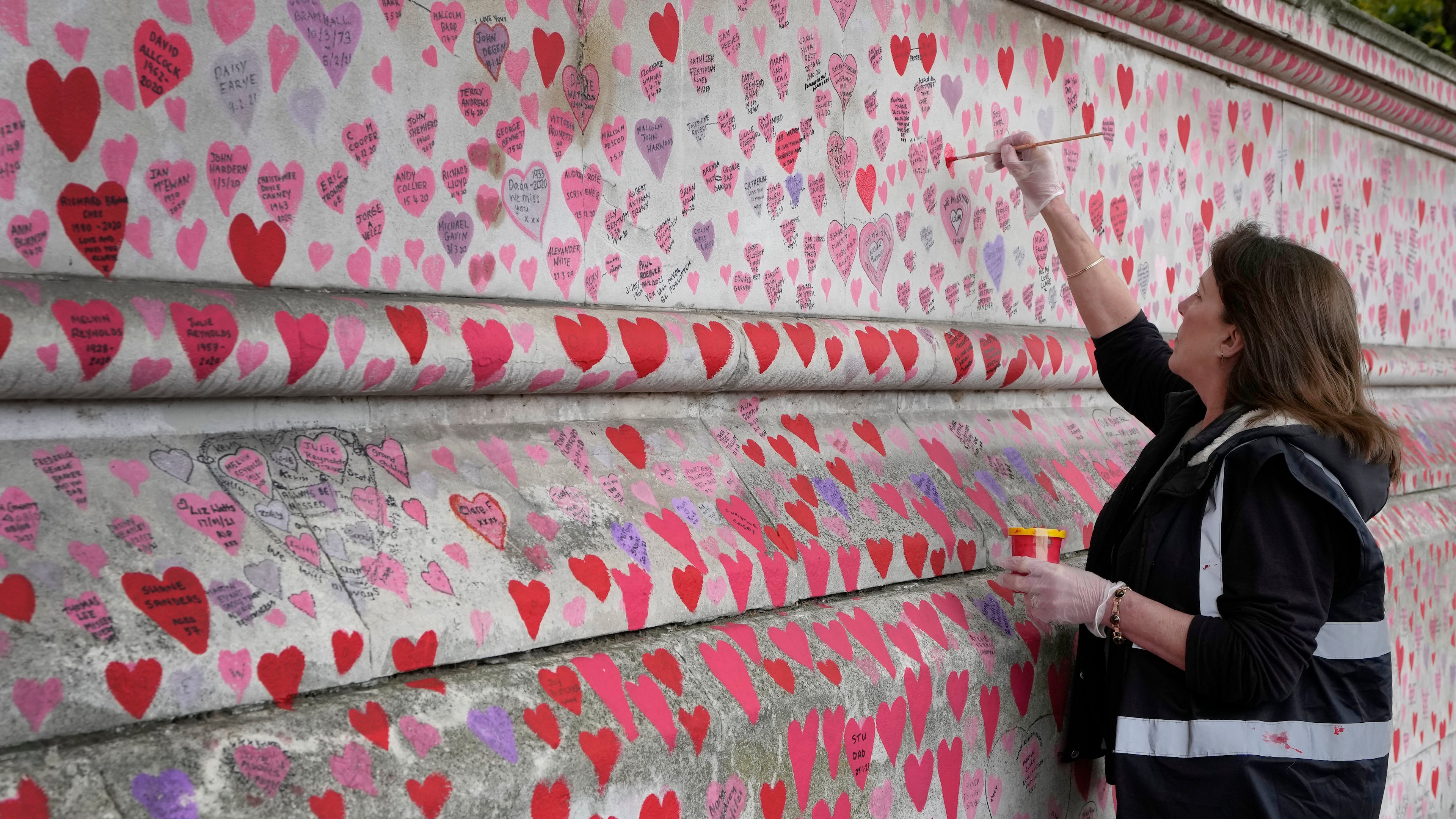 FILE - Volunteer Fran Hall, who lost her husband Steve Mead to COVID-19, re-paints faded hearts on the COVID-19 memorial wall in Westminster in London, Friday, Oct. 15, 2021. (AP Photo/Kirsty Wigglesworth, File)