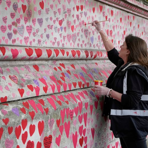 FILE - Volunteer Fran Hall, who lost her husband Steve Mead to COVID-19, re-paints faded hearts on the COVID-19 memorial wall in Westminster in London, Friday, Oct. 15, 2021. (AP Photo/Kirsty Wigglesworth, File)