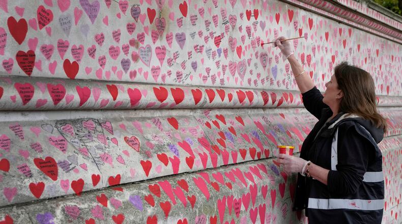 FILE - Volunteer Fran Hall, who lost her husband Steve Mead to COVID-19, re-paints faded hearts on the COVID-19 memorial wall in Westminster in London, Friday, Oct. 15, 2021. (AP Photo/Kirsty Wigglesworth, File)