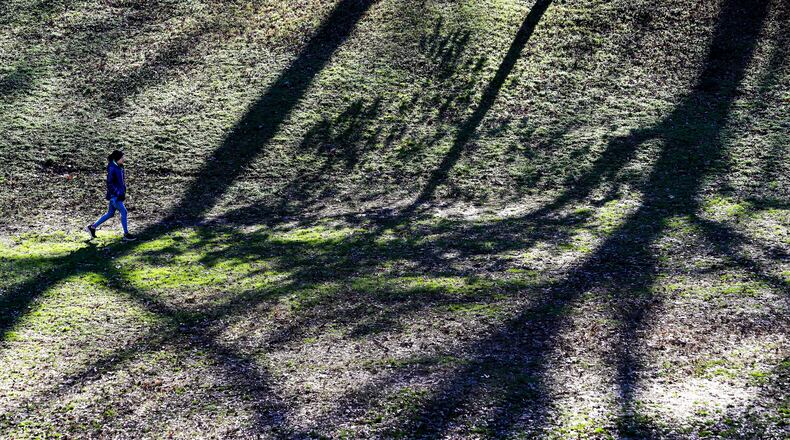 The winter sun cast long shadows across the landscape as Addie Anderson took her dog Rosie (not pictured) for a walk in Wynn Park in Ansley Park in midtown Atlanta on Tuesday. (John Spink / John.Spink@ajc.com)