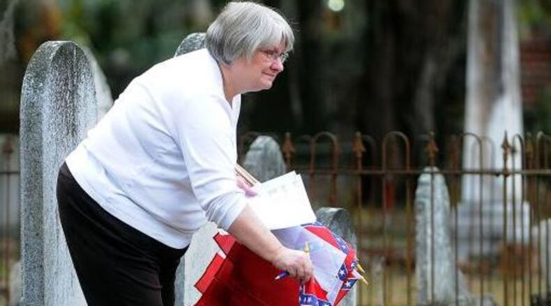 Libby Carter places a Confederate flag replica on a grave at Oak Grove Cemetery in Brunswick. (Credit: Florida Times-Union)