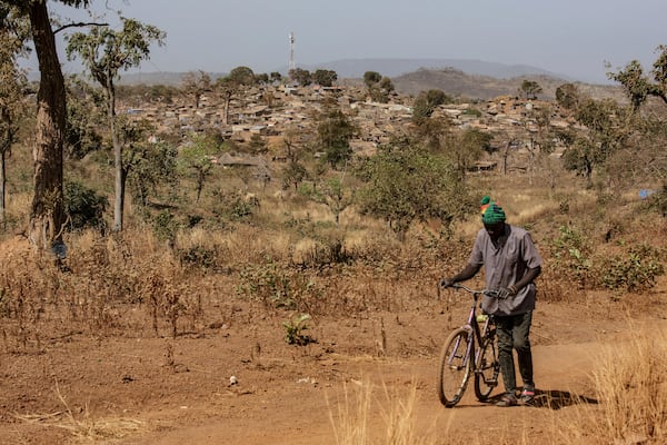 A man walks with his bike with a view of a town built near a gold mining site in the Kedougou region of Senegal on Thursday, Jan. 16, 2025. (AP Photo/Annika Hammerschlag)