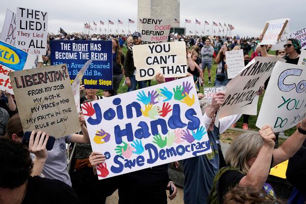Demonstrators hold up signs during a "Hands Off!" protest against President Donald Trump at the Washington Monument in Washington, Saturday, April 5, 2025. (AP Photo/Jose Luis Magana)