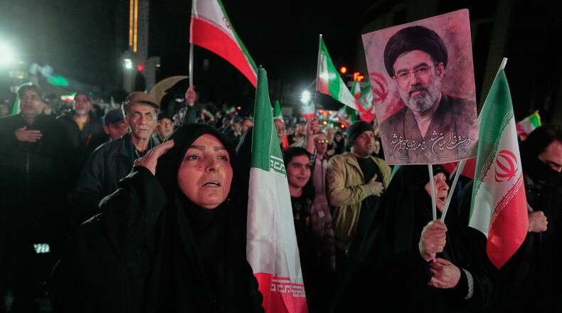 A woman salutes while singing the national anthem as another holds a picture of Iranian Supreme Leader Ayatollah Mojtaba Khamenei during a pro-government gathering in a square in western Tehran, Iran, Wednesday, March 25, 2026. (AP Photo/Vahid Salemi)