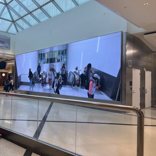 A video screen shows arriving passengers at the top of the escalators at at Hartsfield-Jackson International Airport.
