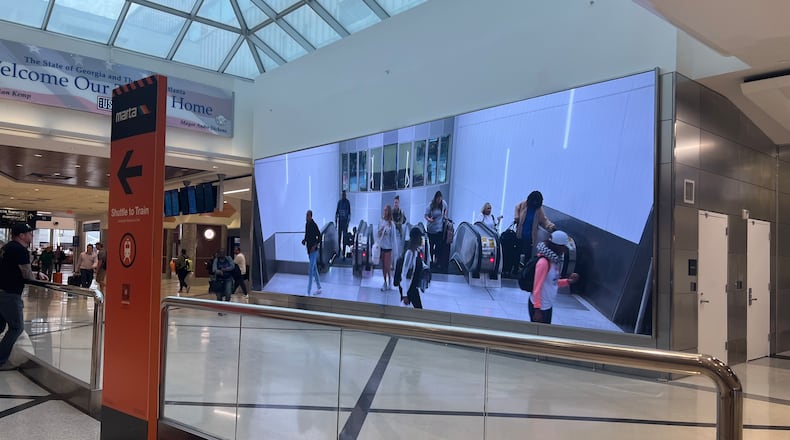 A video screen shows arriving passengers at the top of the escalators at at Hartsfield-Jackson International Airport.