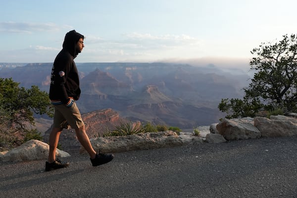 A tourist takes in the morning sunrise from the South Rim as smoke from the Dragon Bravo Fire moves over the Grand Canyon from the North Rim Tuesday, July 15, 2025, in Grand Canyon National Park, Ariz. (AP Photo/Ross D. Franklin)