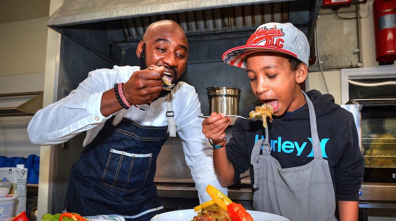Chef Cheikh Ndiaye teaches 12-year-old Fallou Diouf (who is half Senegalese) to cook some of the national dishes of his father’s homeland in the kitchen of Project Community Connections Inc. recently. Here, they are taking a first bite of the Chicken Yassa. CONTRIBUTED BY CHRIS HUNT PHOTOGRAPHY