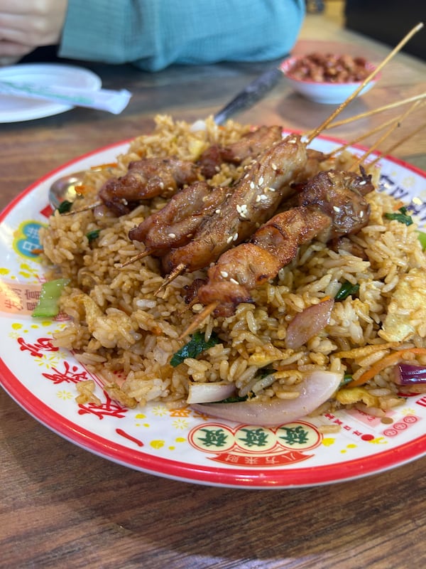 Several meat skewers sit on top of a mound of a fried rice