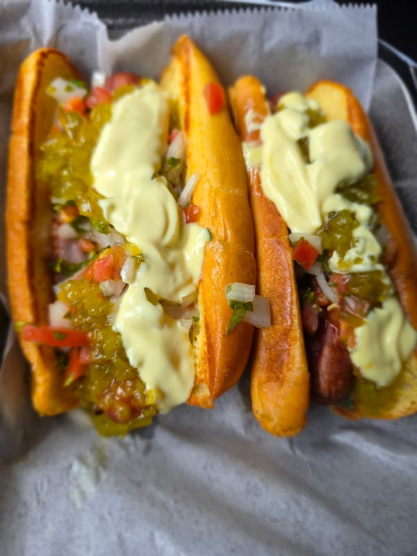Two loaded hot dogs loaded with sauces and peppers.