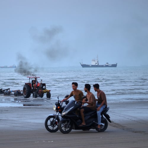 Young men ride motorcycles along the shore as a tractor pulls equipment from the water and commercial vessels appear anchored in the Strait of Hormuz off Bandar Abbas, Iran, Monday, July 27, 2026. (Razieh Poudat/ISNA via AP)
