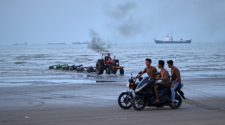 Young men ride motorcycles along the shore as a tractor pulls equipment from the water and commercial vessels appear anchored in the Strait of Hormuz off Bandar Abbas, Iran, Monday, July 27, 2026. (Razieh Poudat/ISNA via AP)