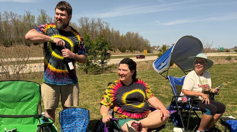 Matt Huggins, left, of Marietta, opens a bottle of wine to celebrate Monday’s total eclipse in Poplar Bluff, Missouri. His wife Katie, and mother-in-law Laura Stokes are seated next to him. (Charles Minshew / AJC)