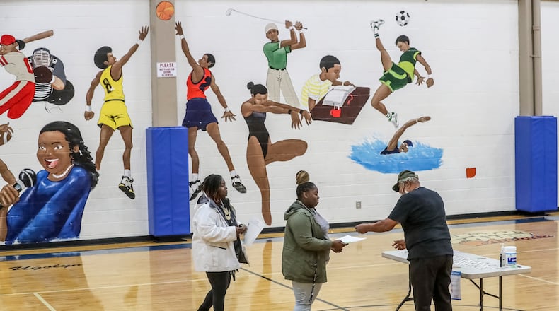 Poll worker Tracy Singletary (right) takes ballots and gives stickers to voters on Tuesday, Dec. 6, 2022 at the Dunbar Neighborhood Center in Atlanta. (John Spink / John.Spink@ajc.com)