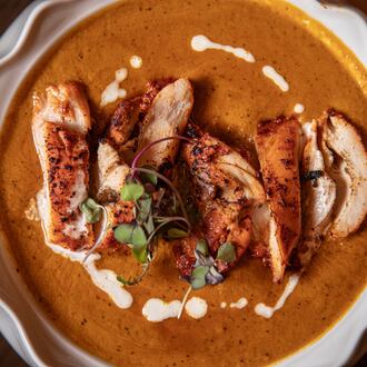 Overhead shot of a decorative plate holding a serving of butter chicken, with sliced pieces of chicken in a thick, red gravy with.a swirl of white sauce.