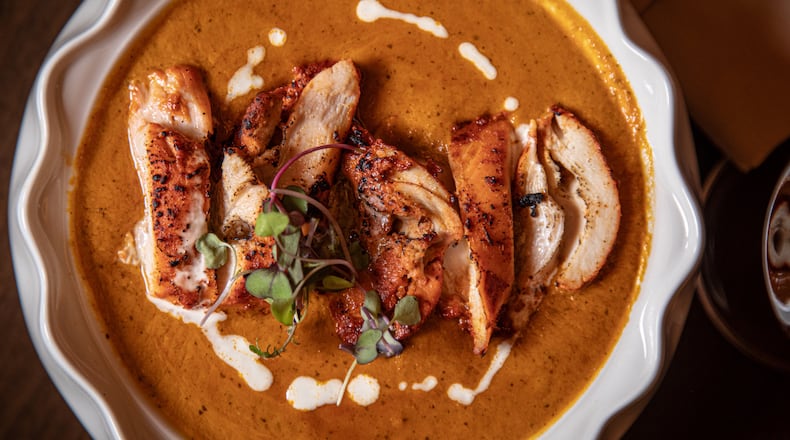 Overhead shot of a decorative plate holding a serving of butter chicken, with sliced pieces of chicken in a thick, red gravy with.a swirl of white sauce.