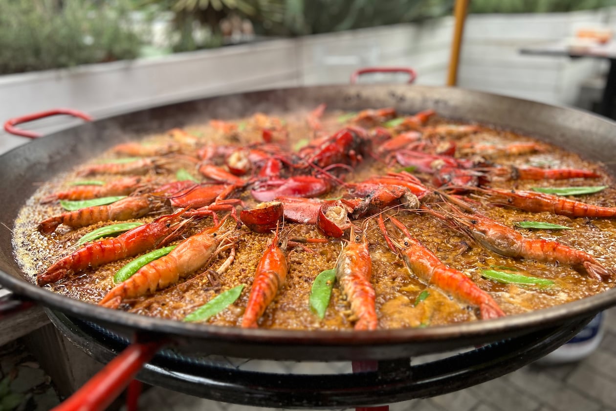 Paella pan filled with rice, shrimp, lobster, and snow peas.