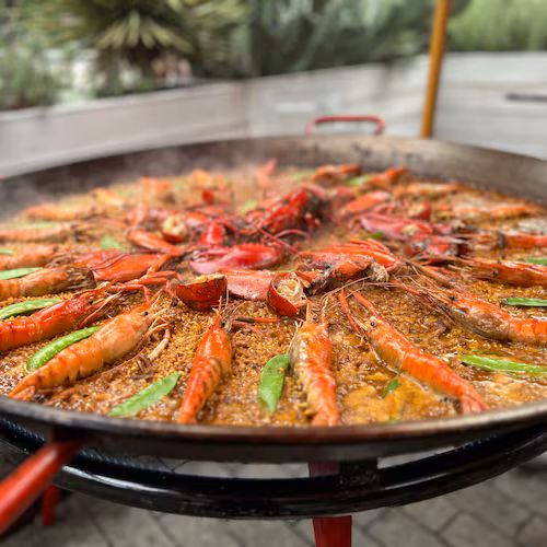 Paella pan filled with rice, shrimp, lobster, and snow peas.