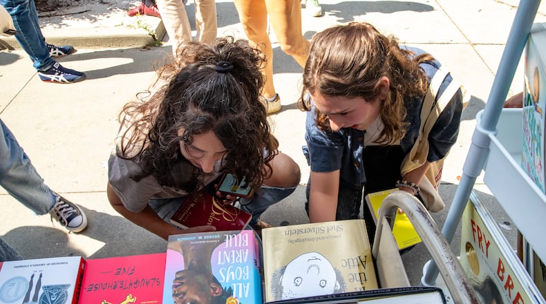 MoveOn Political Action's Banned Bookmobile distributes free banned books at the kickoff of National Banned Book Week where Shereen Mendelson (left) and Isabella Lipham take a look at a few of the banned books that cannot be checked out at public school libraries on Oct. 1, 2023, at Little Shop of Stories in Decatur Square. (Jenni Girtman for the AJC)